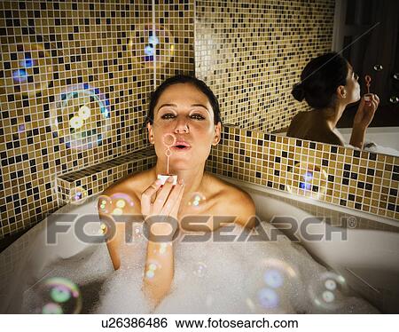 Stock Photograph - Woman in bath blowing bubbles.. Fotosearch
