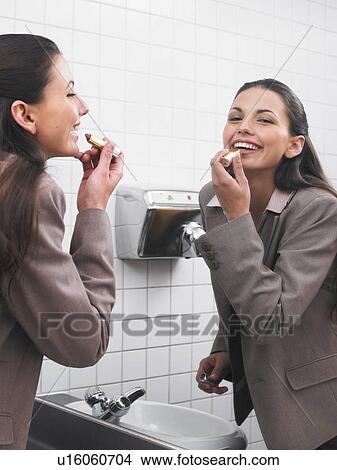 Picture - Woman reflected in office washroom mirror applying make-up. Fotosearch