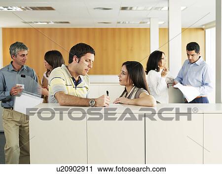 Stock Image - Business colleagues talking to each other in office. Fotosearch