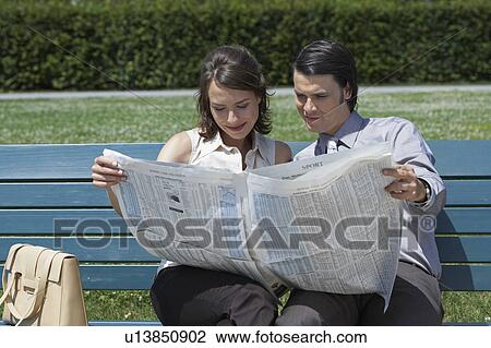 Businessman and woman on bench in park reading a newspaper together. View Large Photo Image Stock Image - Businessman and woman on bench in park reading a newspaper together.. Fotosearch