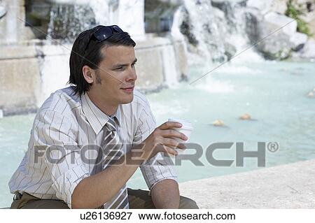 Businessman sitting on edge of fountain holding a coffee to go smiling portrait. View Large Photo Image Stock Photo - Businessman sitting on edge of fountain holding a coffee to go smiling portrait.. Fotosearch