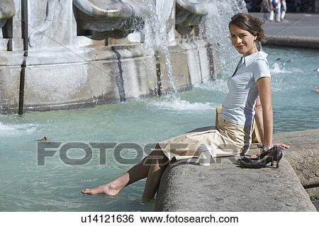Stock Photograph - Businesswoman sitting on edge of fountain bare feet in fountain smiling.. Fotosearch