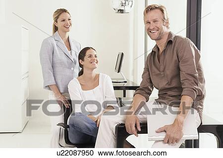 Man and two women in office man seated on desk. View Large Photo Image Stock Image - Man and two women in office man seated on desk.. Fotosearch
