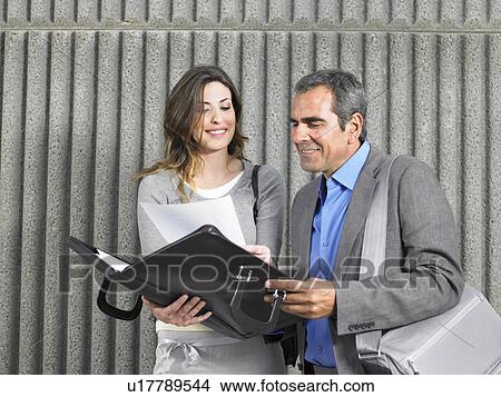 Picture - Older man and young woman looking into document case against textured concrete, Alicante, Spain,. Fotosearch