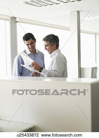 Stock Image - Two businessmen discussing file in office. Fotosearch
