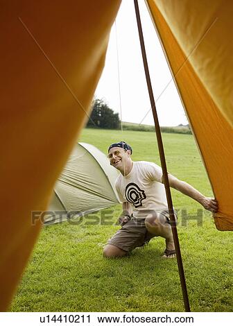 Stock Image - Man setting up a tent and laughing. Fotosearch