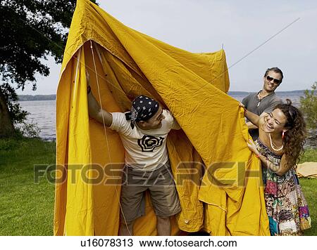 Stock Image - Three people setting up a tent. Fotosearch