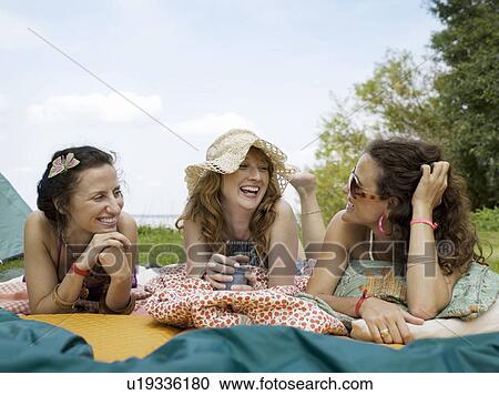 Stock Image - Three women laying on blankets talking. Fotosearch