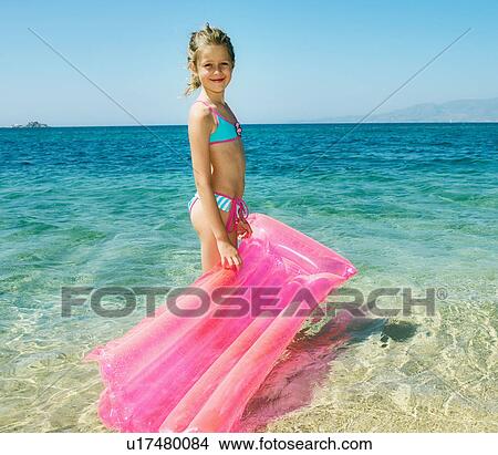 Picture - Young girl holding an inflatable raft at the beach smiling.. Fotosearch