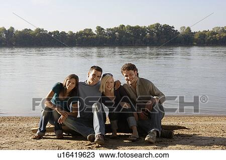 Four friends sitting on log by a lake smiling. View Large Photo Image Stock Image - Four friends sitting on log by a lake smiling.. Fotosearch