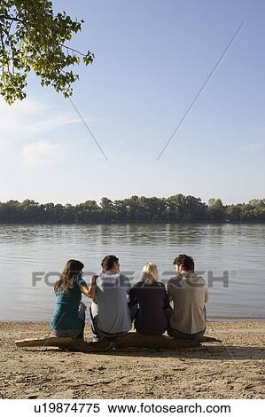 Four friends sitting on log by a lake. View Large Photo Image Stock Photography - Four friends sitting on log by a lake.. Fotosearch