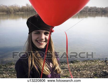 Girl (10-12) standing by river holding red balloon, smiling, portrait View Large Photo Image Stock Photograph - Girl (10-12) standing by river holding red balloon, smiling, portrait. Fotosearch