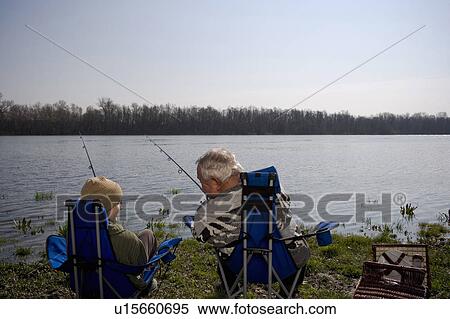 Stock Photography - Grandfather and grandson (12-14) fishing by river, rear view. Fotosearch