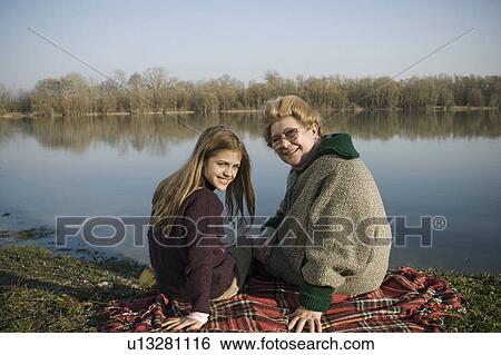 Grandmother and granddaughter (10-12) sitting on rug by river, smiling View Large Photo Image Stock Photograph - Grandmother and granddaughter (10-12) sitting on rug by river, smiling. Fotosearch