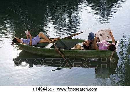Stock Photo - Man and woman lying down and reading in a boat. Fotosearch