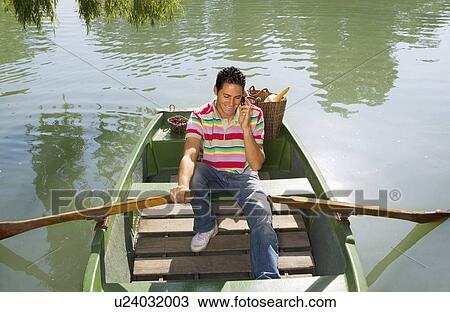 Stock Image - Man with cell phone rowing a boat. Fotosearch