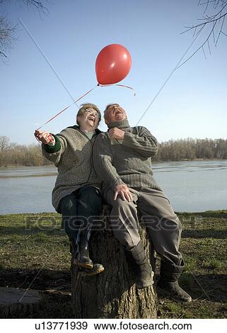 Senior couple sitting by river holding red balloon, smiling View Large Photo Image Stock Photo - Senior couple sitting by river holding red balloon, smiling. Fotosearch