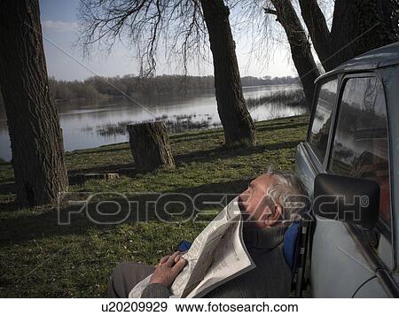 Senior man resting by car on riverside, holding newspaper, eyes closed View Large Photo Image Stock Photo - Senior man resting by car on riverside, holding newspaper, eyes closed. Fotosearch