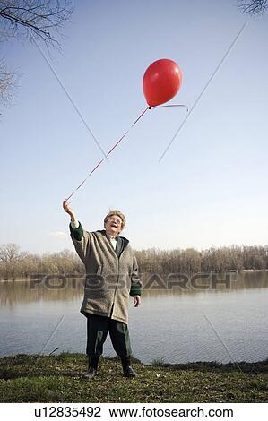 Senior woman standing by river holding red balloon, smiling View Large Photo Image Stock Image - Senior woman standing by river holding red balloon, smiling. Fotosearch
