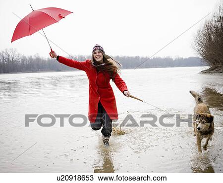 Young woman holding umbrella, running in river with dog, smiling View Large Photo Image Stock Image - Young woman holding umbrella, running in river with dog, smiling. Fotosearch