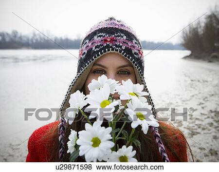 Stock Photo - Young woman outdoors holding flowers up to face, portrait. Fotosearch