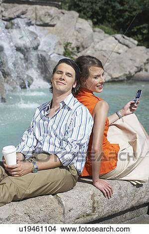 Picture - Businessman and women sitting on fountain's edge while leaning on each other.. Fotosearch