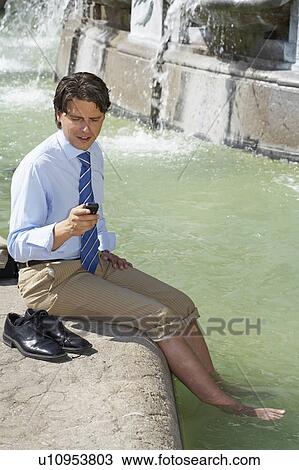 Stock Image - Businessman in fountain on cell phone.. Fotosearch