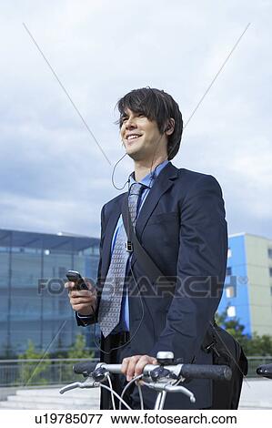 Stock Photo - Businessman in park walking his bike with headset and mobile laughing.. Fotosearch