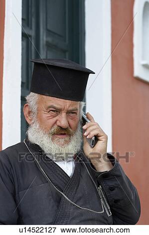 Stock Photo - Old priest in front of church on the mobile.. Fotosearch