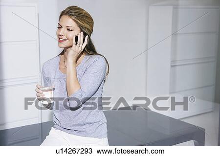 Stock Image - Woman on computer desk on cell phone.. Fotosearch