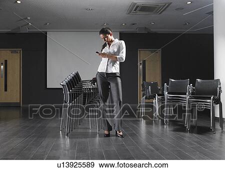 Woman standing with stack of chairs in empty presentation room View Large Photo Image Stock Photo - Woman standing with stack of chairs in empty presentation room. Fotosearch