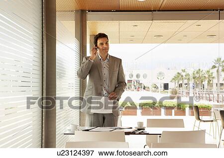 Young business man standing in caf‚ talking on his mobile phone. View Large Photo Image Stock Photo - Young business man standing in caf‚ talking on his mobile phone.. Fotosearch