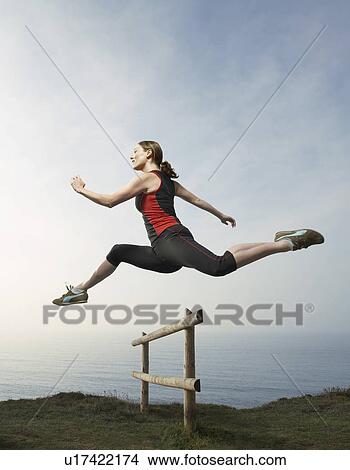 Picture - A woman hurdling a country fence.. Fotosearch