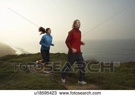 Stock Image - A young couple jogging along a path.. Fotosearch