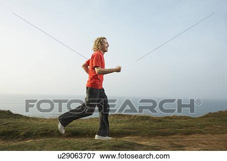 A young Man jogging along a cliff path. View Large Photo Image Stock Photo - A young Man jogging along a cliff path.. Fotosearch