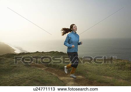 Stock Image - A young Woman jogging along a cliff path.. Fotosearch