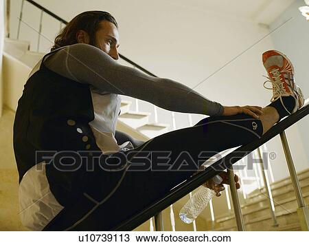 Stock Image - Mature man stretching leg on railing by steps. Fotosearch