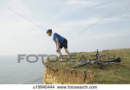 Picture - Cyclist looking over a cliff.. Fotosearch
