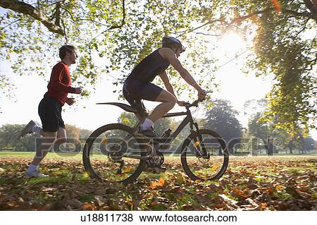 Cyclist riding mountain bike with jogger following. View Large Photo Image Stock Photo - Cyclist riding mountain bike with jogger following.. Fotosearch