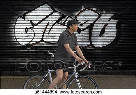 Man on bicycle by graffiti in street, side view View Large Photo Image Picture - Man on bicycle by graffiti in street, side view. Fotosearch
