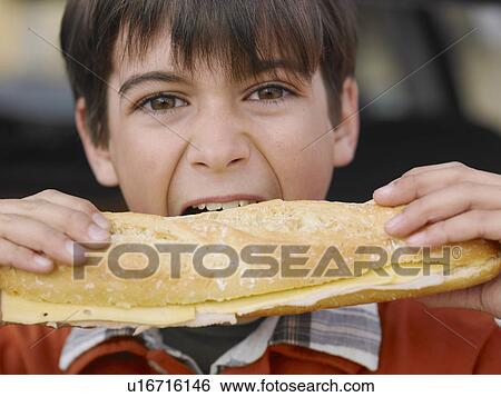 Stock Photograph - Boy (8-10) eating large cheese baguette, close-up, portrait. Fotosearch