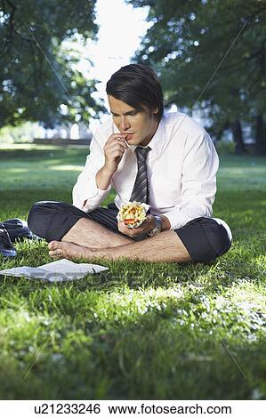 Stock Photograph - Businessman eating in park while reading.. Fotosearch
