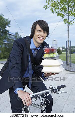 Businessman in park on bike with lots of lunchboxes laughing. View Large Photo Image Stock Photo - Businessman in park on bike with lots of lunchboxes laughing.. Fotosearch