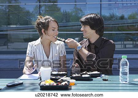 Stock Image - Couple eating sushi together outside while working.. Fotosearch