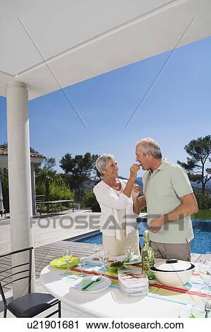 Stock Image - Man and woman eating by poolside.. Fotosearch