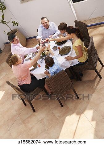Multi generational family toasting glasses at dining table, smiling View Large Photo Image Picture - Multi generational family toasting glasses at dining table, smiling. Fotosearch