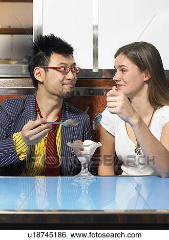 Young couple sharing icecream in cafe smiling at each other View Large Photo Image Stock Photograph - Young couple sharing icecream in cafe smiling at each other. Fotosearch