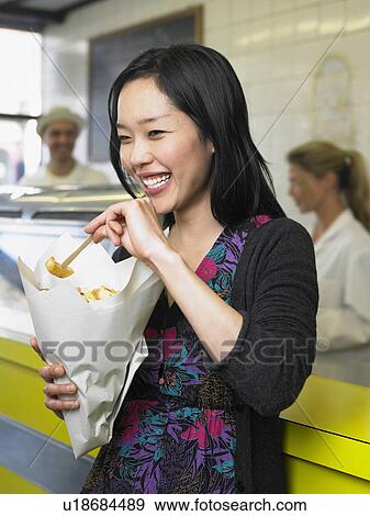 Young woman eating chips in fish and chip shop smiling View Large Photo Image Stock Photo - Young woman eating chips in fish and chip shop smiling. Fotosearch