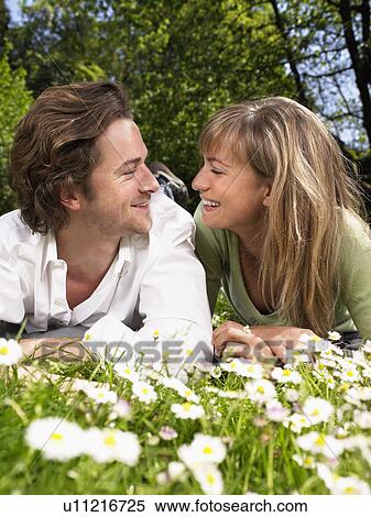 Couple lying in the grass smiling at each other. View Large Photo Image Stock Photography - Couple lying in the grass smiling at each other.. Fotosearch