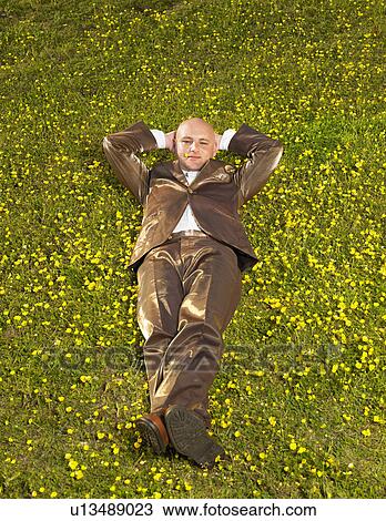 Stock Image - Man lying on grass in gold suit.. Fotosearch